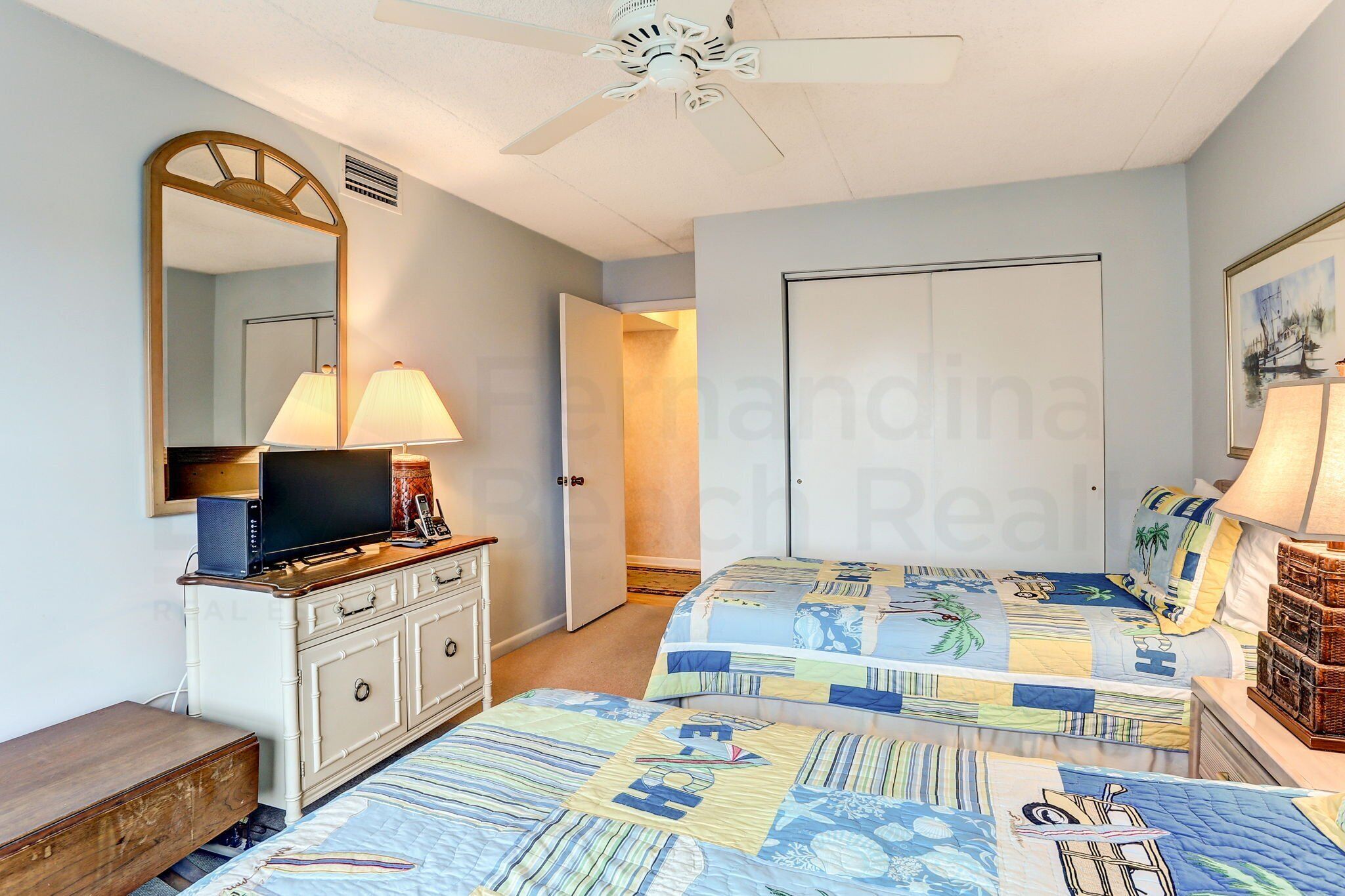 A bedroom with two beds, a TV, a dresser, and a ceiling fan.