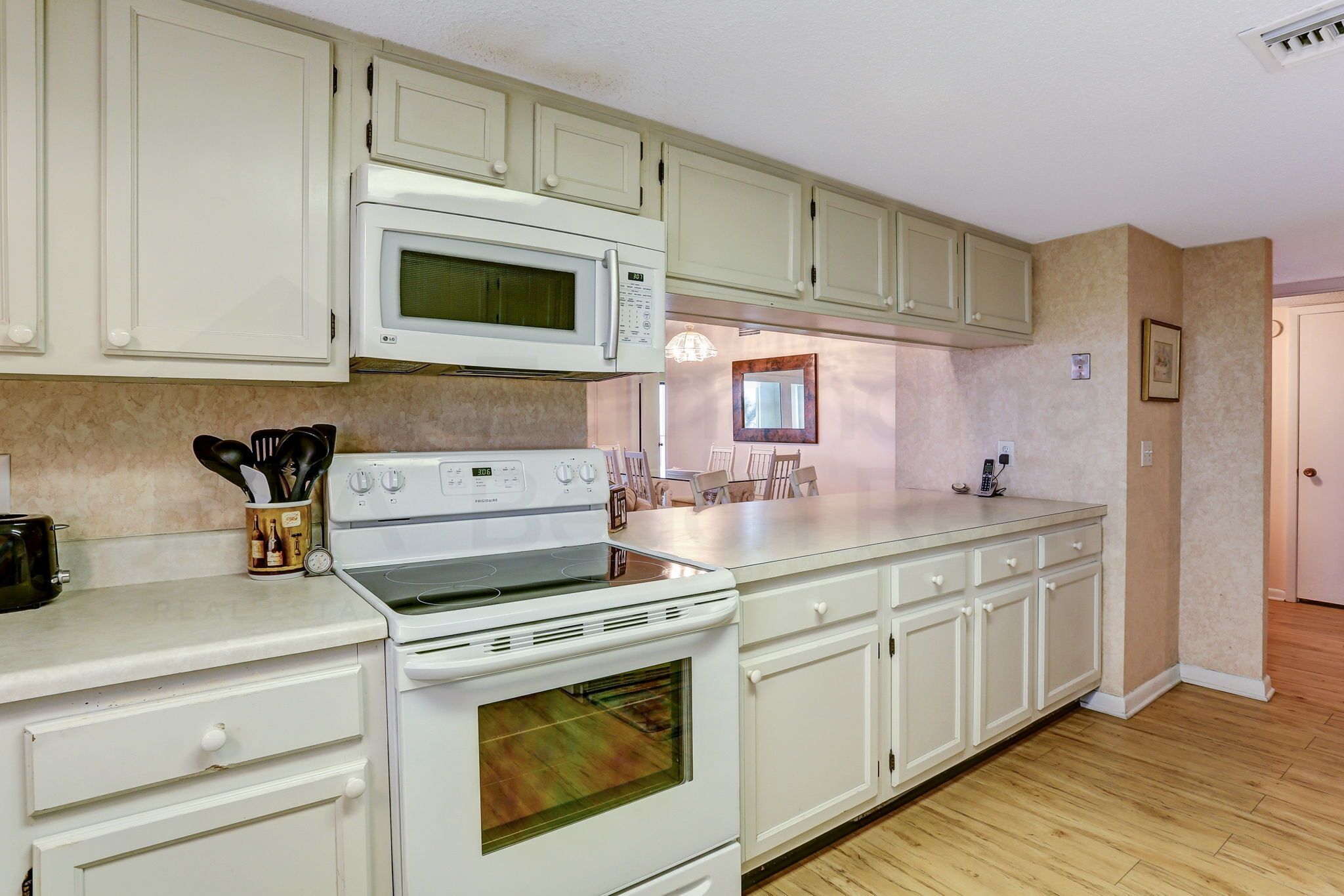 Una cocina con armarios blancos, microondas, estufa y horno. Se ve una ventana con vistas al exterior.
