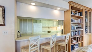 A kitchen with a bar area, white cabinets, and a bookshelf filled with books. - 301 Atlantis (Fernandina Beach)