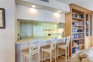 A kitchen with a central island, white bar stools, a wooden bookshelf, and a white refrigerator.