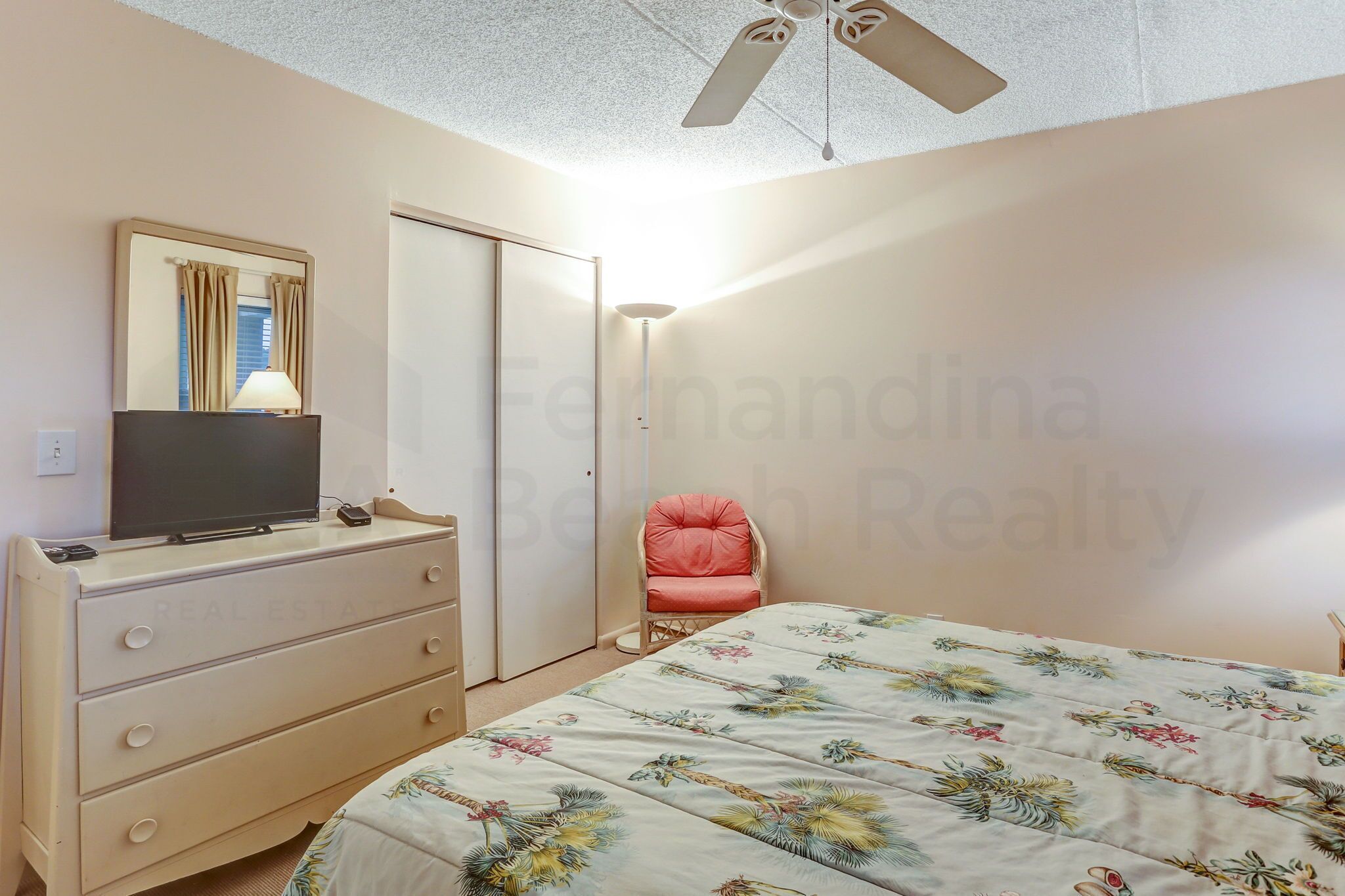 A bedroom with a bed, a dresser, a television, a chair, and a ceiling fan.