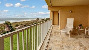 A balcony with a view of the beach, a chair, a small table, and a potted plant. - 301 Atlantis (Fernandina Beach)