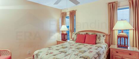 A bedroom with a bed, nightstands, a lamp, a ceiling fan, and a window with curtains.