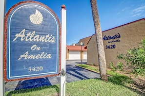Ein blauer Briefkasten mit der Aufschrift 'Atlantis on Amelia 3420', ein Gebäude mit der Inschrift 'Atlantis on Amelia 3420' an der Wand und ein klarer Himmel.