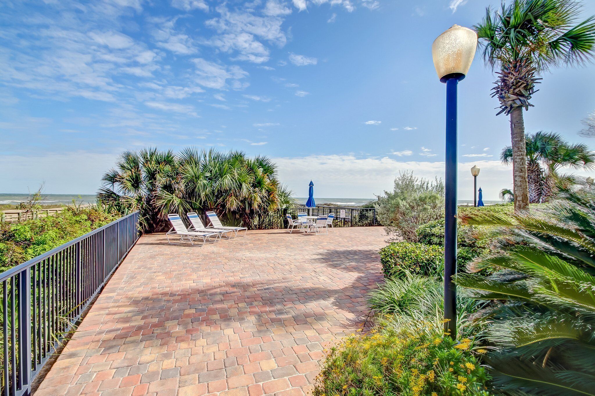 A paved patio with lounge chairs and a view of the ocean.