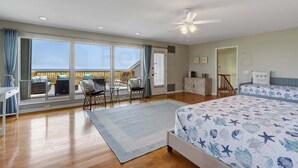 Ein Schlafzimmer mit einem großen Bett, einem Schreibtisch, einem Sessel und einem Balkon mit Blick.