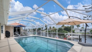 Una piscina con cerramiento de vidrio, sillas de descanso y sombrillas.