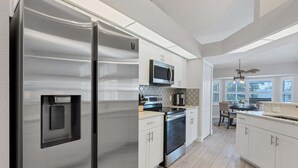 Una cocina moderna con electrodomésticos de acero inoxidable, armarios blancos y un comedor con luz natural.