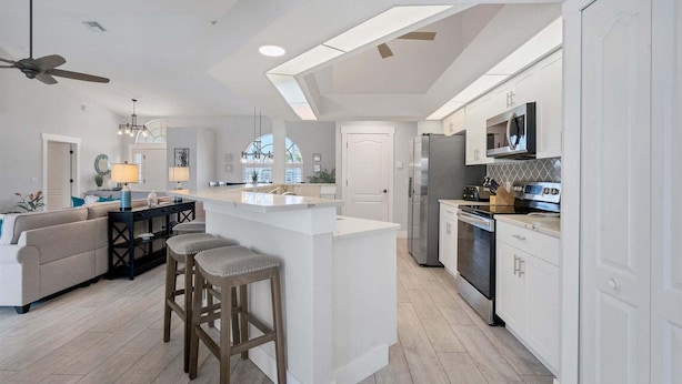 Una cocina moderna con una isla central, una zona de comedor con sofá y sillas, y un ventilador de techo.