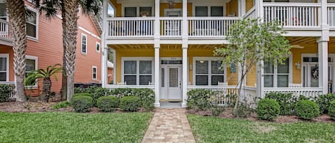 A two-story building with a central entrance, a covered porch, and a brick pathway leading to the door.