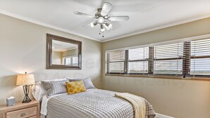 A bedroom with a bed, nightstand, lamp, ceiling fan, window blinds, and a mirror. - 6th Floor, Updated and Beautiful! Oceanfront Condo With Balcony, Fishing Pier (Fernandina Beach)