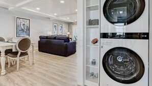 A modern living room with a dining area, a black sofa, and a white washing machine with shelves.