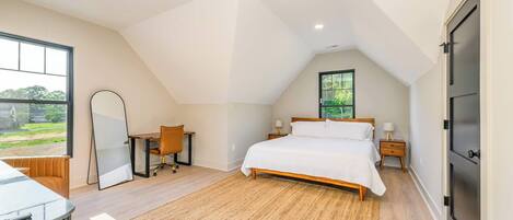 A bedroom with a sloped ceiling, a bed, a desk, and a chair.
