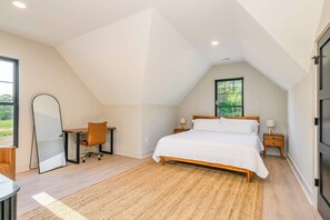 A bedroom with a large bed, a desk with a chair, a mirror, and a window with a view of greenery. - Energetic Lakeview Loft (Mooresville)