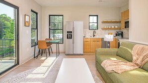 A modern kitchen with a refrigerator, stove, and microwave. There is a dining area with a table and chairs, and a green sofa in the living room.
