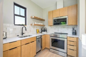 Une cuisine moderne avec des meubles en bois, une cuisinière en acier inoxydable, un four encastré, une machine à café et une fenêtre au-dessus de l’évier.