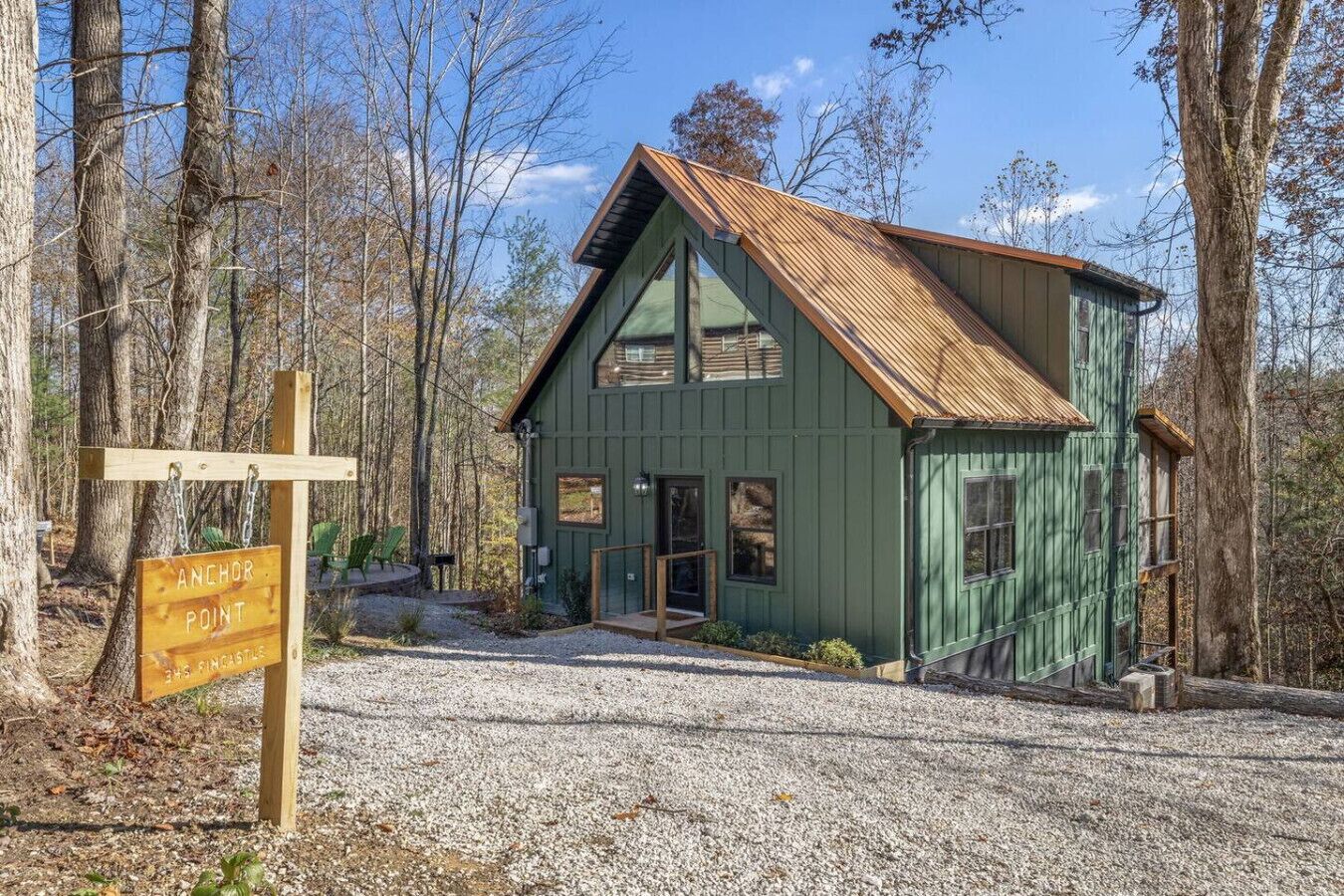 A rustic cabin with a green exterior and a sloped roof, surrounded by trees.