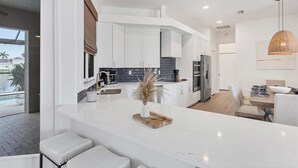 A modern kitchen with white cabinetry, a central island, and a dining area with a table and chairs. - Fpc228 (Punta Gorda)
