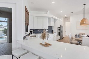 A modern kitchen with white cabinetry, a central island, and a dining area with a table and chairs. - Fpc228 (Punta Gorda)