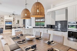 Una cocina moderna con armarios blancos, una isla grande y un comedor con una mesa de madera dispuesta para seis comensales.