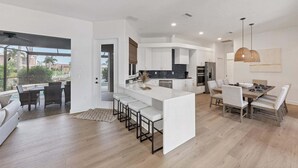 A modern kitchen with white cabinetry, a central island, and a dining area with a table and chairs. - Fpc228 (Punta Gorda)
