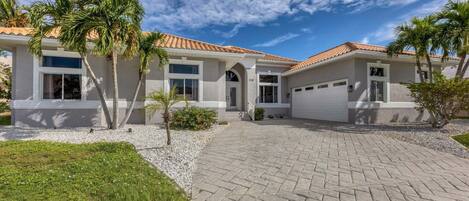 A two-story house with a tiled roof, a driveway, and palm trees.