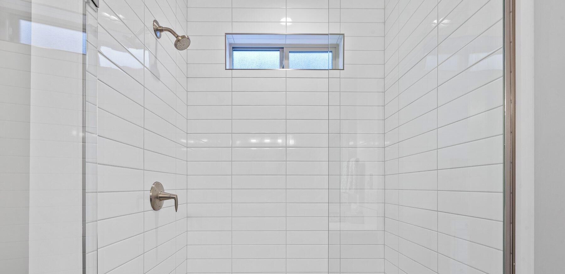 A modern shower with white tiles, a window, and a showerhead.