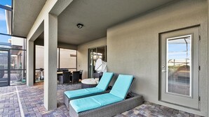 A covered outdoor area with two wicker lounge chairs with blue cushions, a table with chairs, and a door with a window. - Rhs9030 (Kissimmee)
