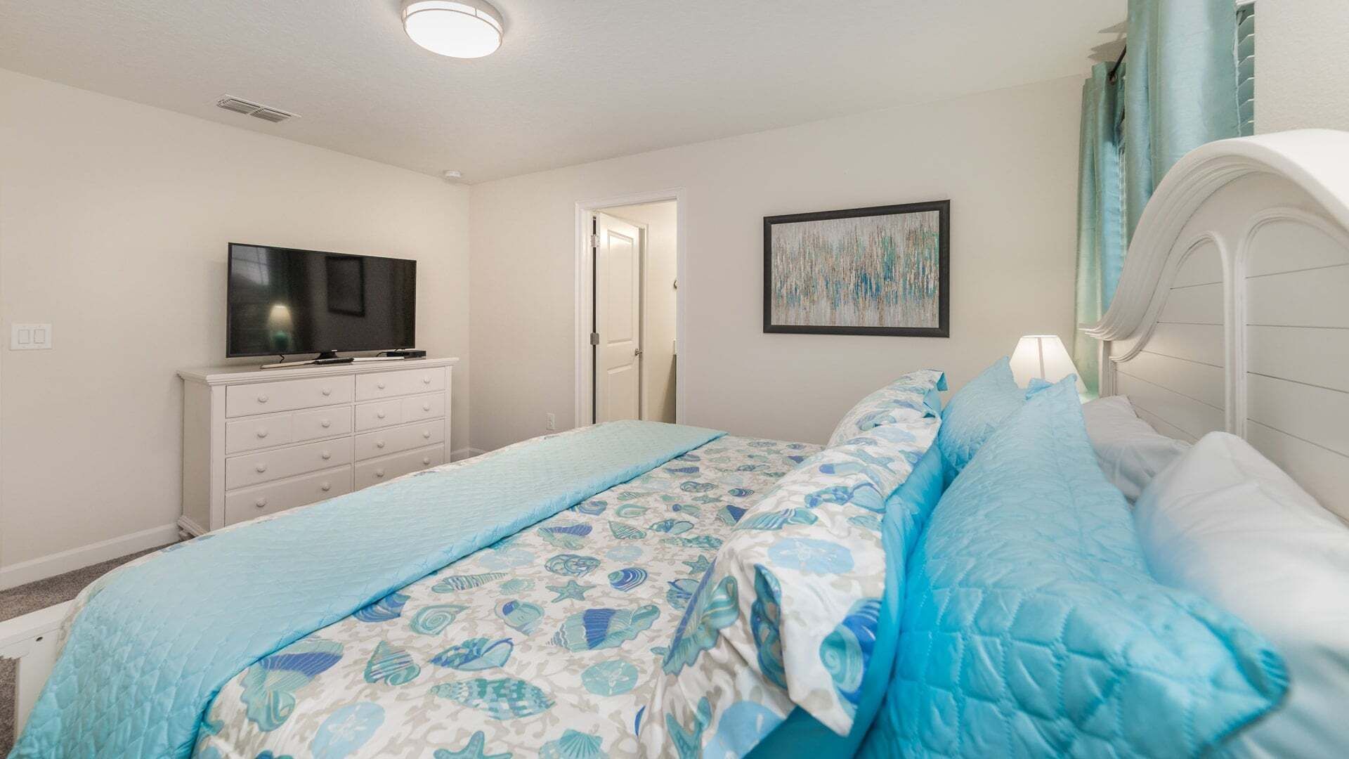 A bedroom with a bed, a dresser, a television, and a door.