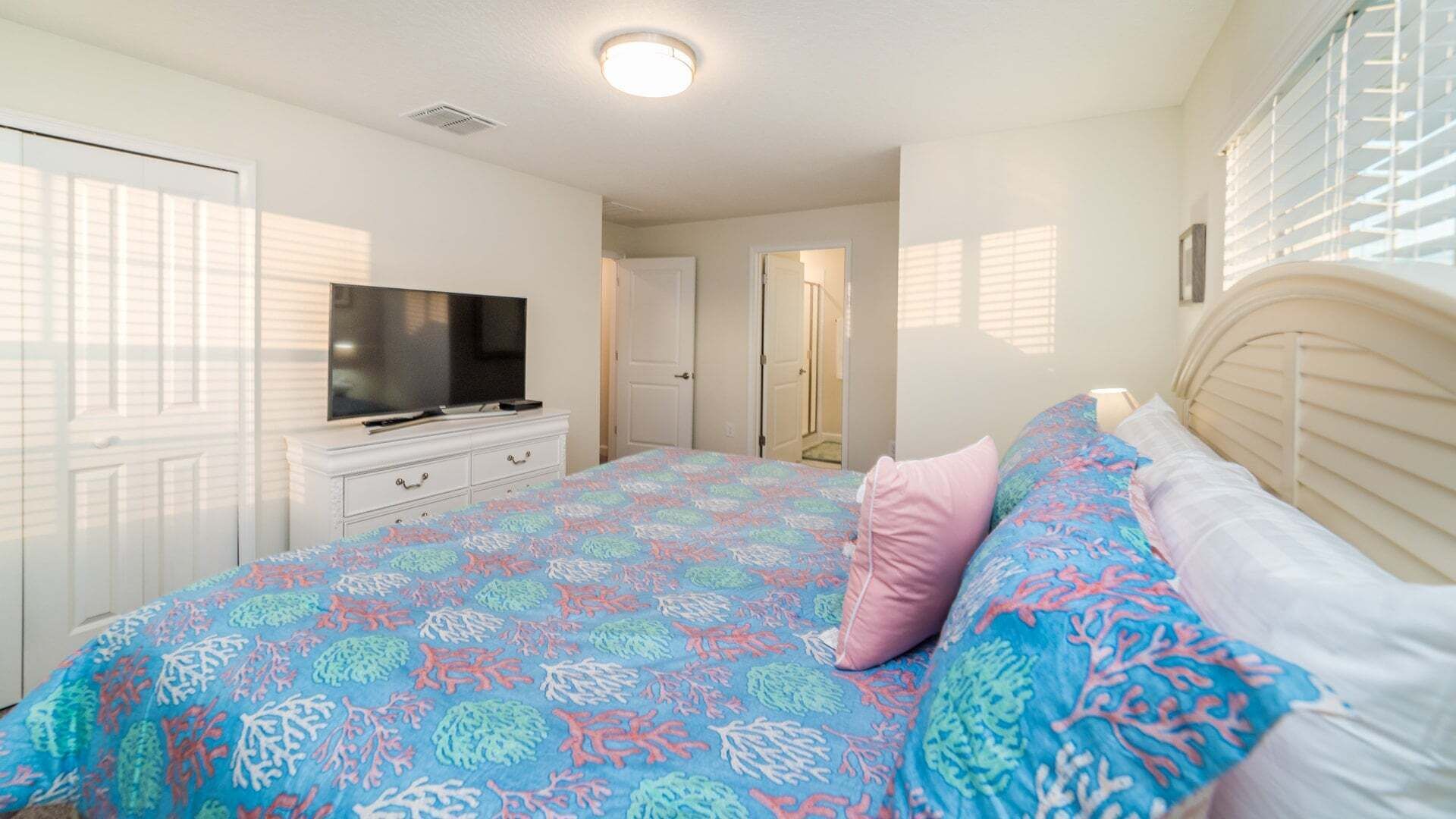 Ein Schlafzimmer mit einem Bett, einem Fernseher auf einer Kommode und einer Tür zu einem anderen Raum.