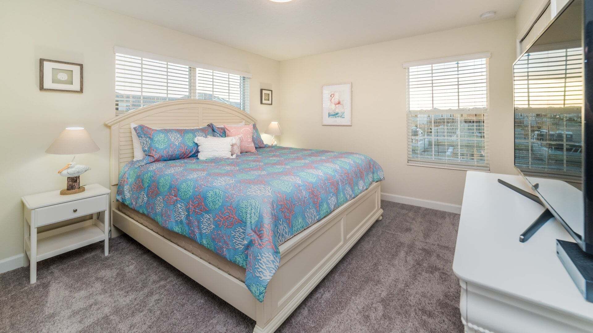 Un dormitorio con cama, mesitas de noche, un escritorio y ventanas.