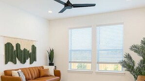 A modern living room with a brown leather sofa, a grey rug, a ceiling fan, and two windows with blinds. - Relaxing Getaway, Worker-friendly, A+ Location (Sherman)