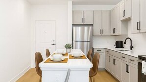 A modern kitchen with white cabinets, a stainless steel refrigerator, and a dining area with a table set for two. - Relaxing Getaway, Worker-friendly, A+ Location (Sherman)