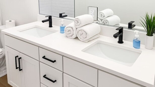 Ein Badezimmer mit zwei Waschbecken, einem Spiegel, Handtüchern, einer Seifenspender und einem Blumentopf.