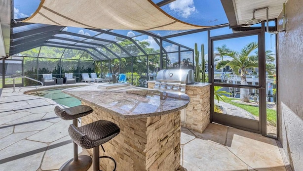 Un espacio al aire libre techado con piscina, taburetes de bar y una parrilla.
