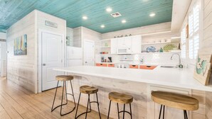 Une cuisine moderne avec des meubles blancs, un grand îlot central doté de tabourets et un plafond bleu.