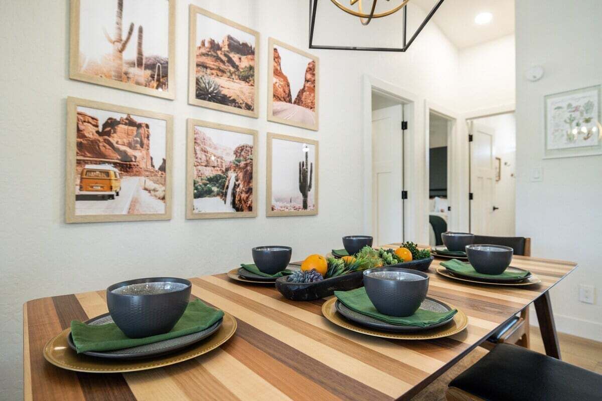 A dining area with a wooden table set for four, surrounded by framed desert landscape pictures.