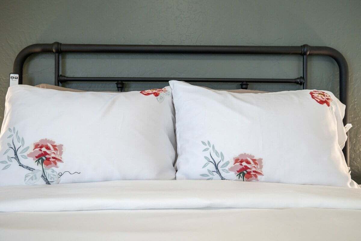 Una cama con cabecera de metal y dos almohadas con bordado floral.