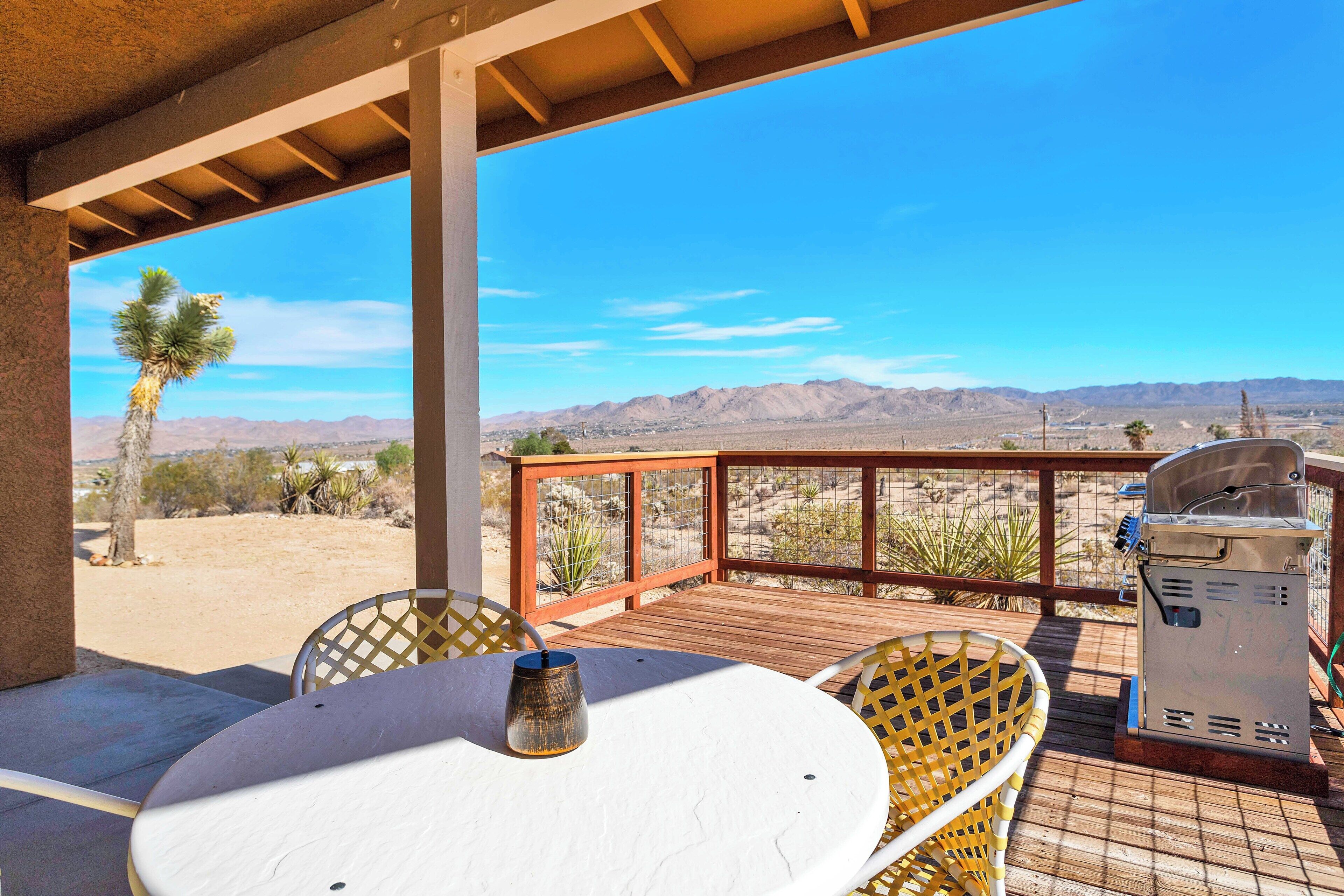 A patio with a table and chairs, a grill, and a view of desert mountains.