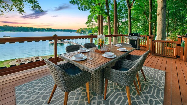 A wooden deck with a dining table set for four, surrounded by wicker chairs, overlooking a lake with boats. - Normandy Approach (Mooresville)