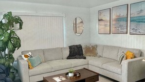A living room with a sectional sofa, a coffee table, a large plant, and three framed pictures on the wall. - Quaint Mid-century Cottage by the Coast (Ventura)