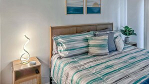 A bedroom with a bed, a nightstand, a wall-mounted lamp, and a potted plant. - Quaint Mid-century Cottage by the Coast (Ventura)