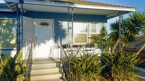 A two-story house with a covered porch, a front door, and a small outdoor seating area with a table and chairs. - Quaint Mid-century Cottage by the Coast (Ventura)