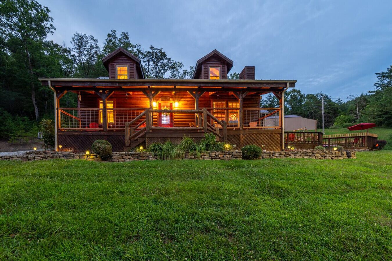 A log cabin with a covered porch, a stone foundation, and a small deck area.