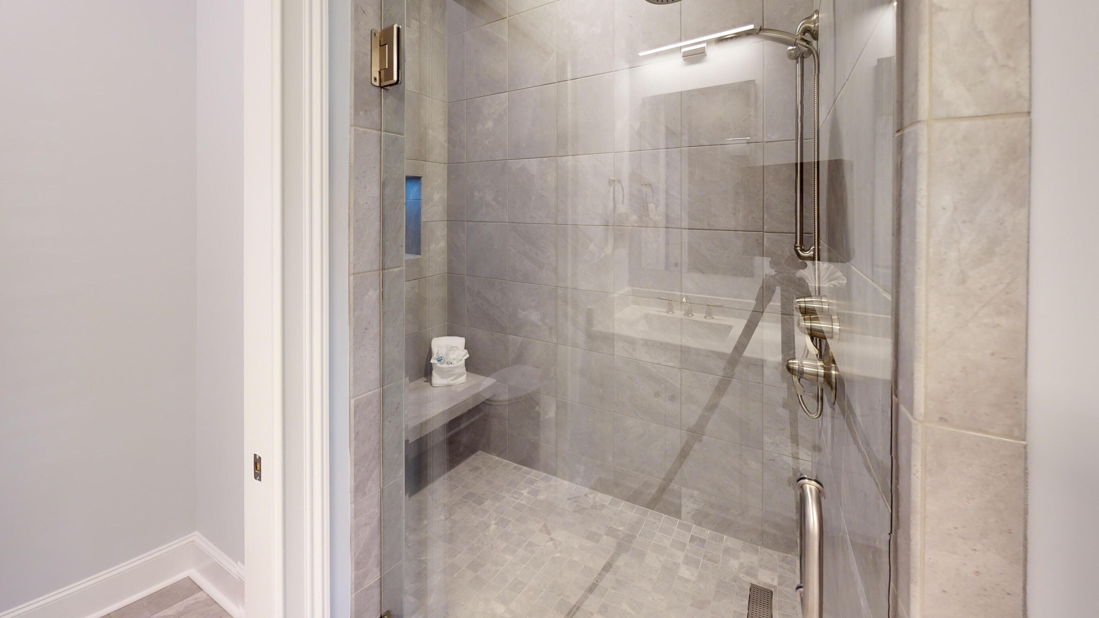 Una doccia a filo pavimento con porta in vetro, un water e uno scaffale con articoli da toilette.