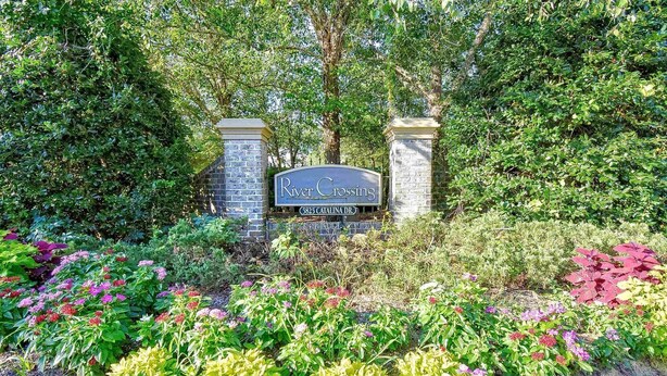 A sign for River Crossing at 5825 Catalina Dr. surrounded by lush greenery and colorful flowers. - River Crossing 231 (North Myrtle Beach)