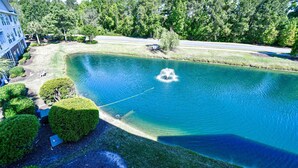 A large, clear pond with a fountain in the center, surrounded by well-maintained lawns and trees. - River Crossing 231 (North Myrtle Beach)