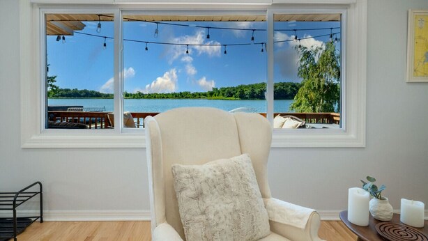 A room with a large window overlooking a lake, a cushioned chair, and a small table with candles.