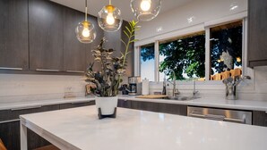 A modern kitchen with a large island, pendant lights, and a view of trees outside.