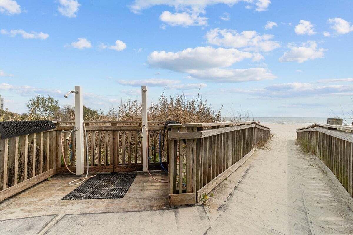 A wooden boardwalk leading to a beach with a metal structure and a hose on the left.